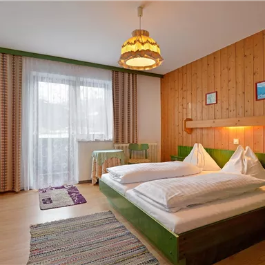A cozy bedroom with a double bed and wood paneling. The room is bright and welcoming, with a window that lets in daylight.