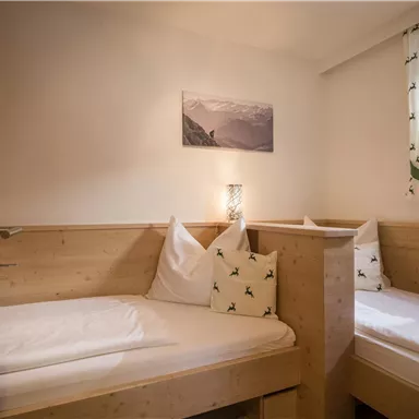 A cozy bedroom with two single beds made of light wood. The walls are neutral, and a window provides daylight.