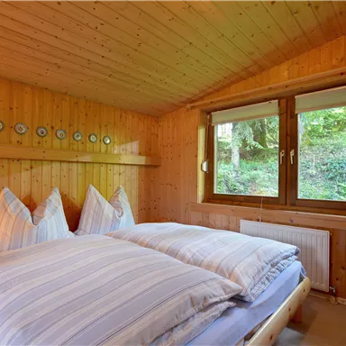 A cozy bedroom with wood paneling and two beds. Large windows offer a view of the greenery.