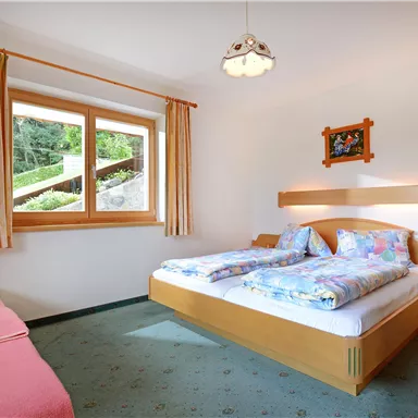 A bright room with two beds and a cozy sofa. Large windows offer a view of nature.