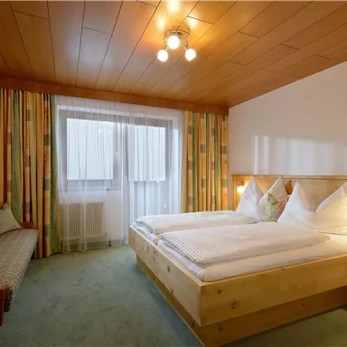 A cozy bedroom with two beds and wooden panels. The room has large windows and colorful curtains.