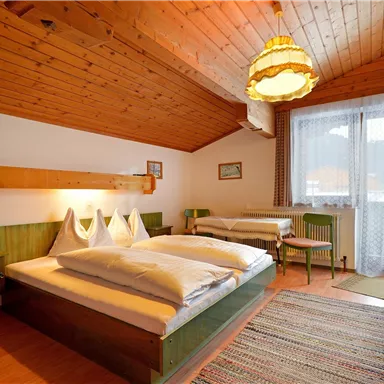 A cozy bedroom with a wooden ceiling and two beds. Additionally, there is a small balcony and warm lighting.