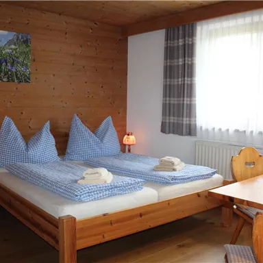 Ein gemütliches Schlafzimmer mit zwei Betten und karierten Bettüberzügen. Der Raum hat Holzverkleidung und einen Tisch mit Blumen.