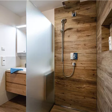 A modern bathroom with a wooden-look shower. There is a sink cabinet and a frosted glass panel.