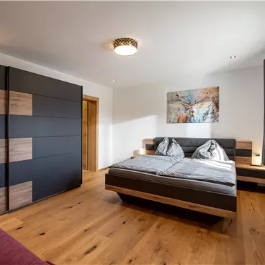 A modern bedroom with a double bed and wooden flooring. The walls are light, and there is a painting above the bed.