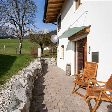 A cozy terrace with two wooden chairs. In the background, there is a green meadow and mountains.