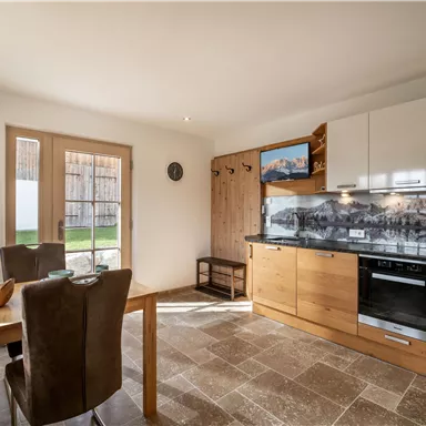 A modern kitchen with wooden details and a dining area. Large windows let in plenty of light and offer a view of the outdoor area.