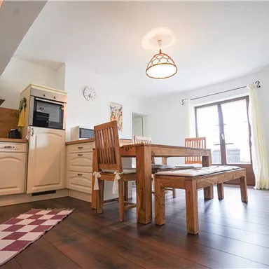 A bright kitchen with modern design and a large wooden dining table. The windows let in plenty of daylight, creating a friendly atmosphere.