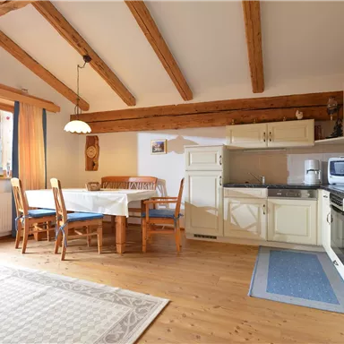 A modern kitchen with wooden beams and a dining table. The room is bright and friendly, with a window that looks out at the mountains.