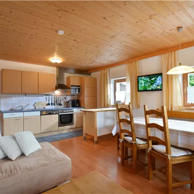 A cozy kitchen with wood decor and a dining table. The room is bright and friendly, with windows and modern kitchen appliances.