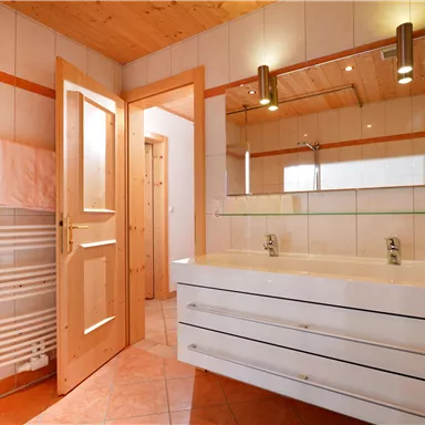 A modern bathroom with a large mirror and a double sink. Bright tiles and a warm wooden ceiling create an inviting atmosphere.