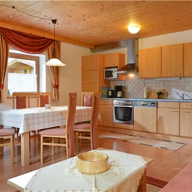 A bright kitchen with wooden shelves and a dining table. Modern appliances and cozy furniture create an inviting atmosphere.