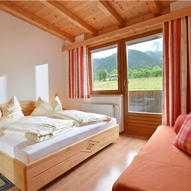 A cozy room with a double bed and a day bed. Large windows offer a view of the mountains and plenty of daylight.