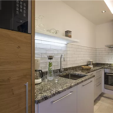 A modern kitchen with granite surfaces and white tiles. It is well equipped with appliances and offers plenty of light.