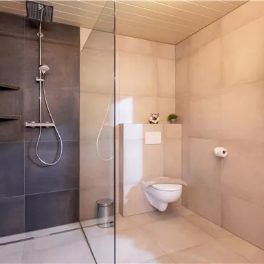 A modern bathroom with an open shower and a gray tiled wall. The toilet is simple and functional, with a window that lets daylight in.