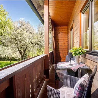 A cozy balcony overlooking a blooming garden. A table with flowers and two chairs invites relaxation.