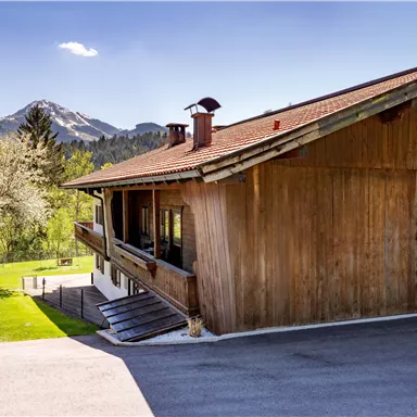 A modern wooden house in the mountains with a beautiful view of the surrounding landscape. The sky is blue and it is a sunny day.
