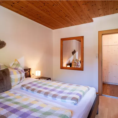 A cozy bedroom with two beds and colorful blankets. In the background, a mirror and a wardrobe can be seen.