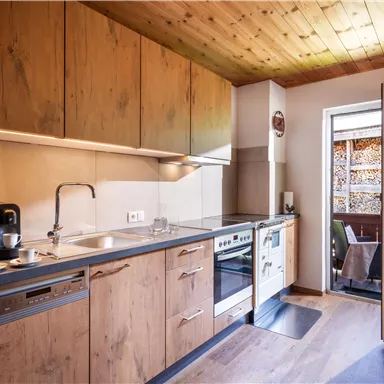 A modern kitchen with wooden cabinets and bright walls. The door opens to a small outdoor area.