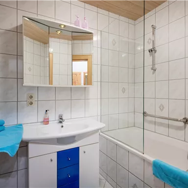 Ein modernes Badezimmer mit weißen Fliesen und einer Badewanne. Auf dem Waschbecken liegen turquoise Handtücher.