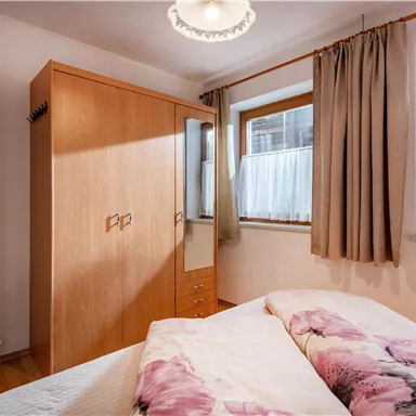 Ein gemütliches Schlafzimmer mit einem großen Bett und Holzmöbeln. Das Zimmer hat Fenster mit Vorhängen und eine angenehme Beleuchtung.