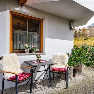 Ein gemütlicher Außenbereich mit einem Tisch und zwei Stühlen, dekoriert mit Blumen. Die Umgebung ist grün und einladend, ideal für entspannte Stunden im Freien.