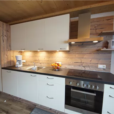 Eine moderne Küche mit hellen Schränken und einer Holzverkleidung. Sie ist gut ausgestattet mit einem Herd, einer Spüle und einigen Küchenutensilien.