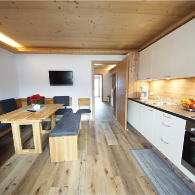 Eine moderne Wohnung mit einem gemütlichen Essbereich und einer gut ausgestatteten Küche. Der Holzfußboden und die natürlichen Materialien schaffen eine einladende Atmosphäre.