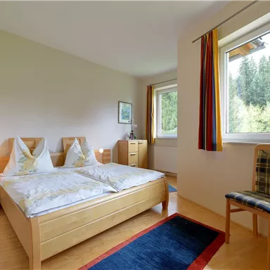 Ein gemütliches Schlafzimmer mit zwei Einzelbetten, einem Stuhl und Fenster, die Blick ins Grüne bieten. Der Raum ist hell und freundlich gestaltet.