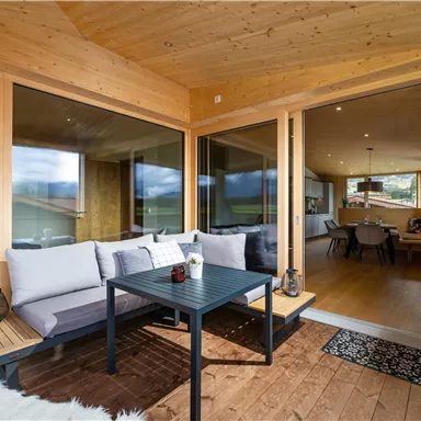 Ein gemütlicher Balkon mit modernen Möbeln und großen Fenstern. Der Raum bietet einen Blick auf die Natur und einen einladenden Wohnbereich.