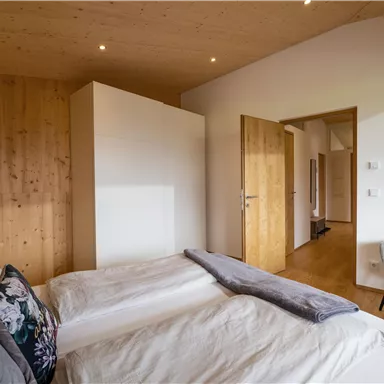 Ein modernes Schlafzimmer mit Holzverkleidung und einem großen Fenster. Das Zimmer ist hell und gemütlich eingerichtet, mit einem Doppelbett und einem Stuhl.