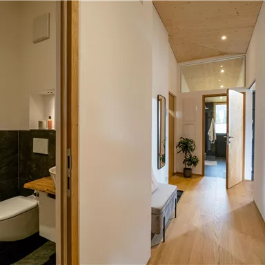Ein moderner Flur mit einer offenen Tür und Holzfußboden. Auf der linken Seite ist ein kleines Badezimmer mit eleganten Akzenten.