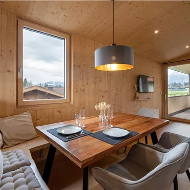 Ein gemütlicher Essbereich aus Holz mit einem großen Tisch und modernen Stühlen. Das Zimmer hat große Fenster und bietet einen Blick auf die Natur.