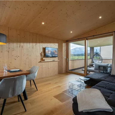 Ein modernes Wohnzimmer mit Holzinterieur und großem Fenster. Es gibt einen Esstisch und eine gemütliche Sitzgelegenheit.