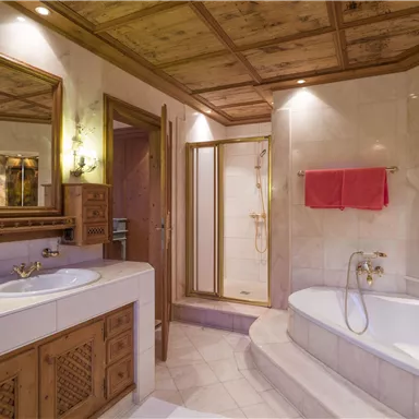 An elegant bathroom with wooden ceilings and modern fixtures. It features a bathtub and a shower cabin, as well as a large mirror.