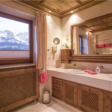 A stylish bathroom with wood paneling and a bathtub. Through the window, there is a view of snow-covered mountains.