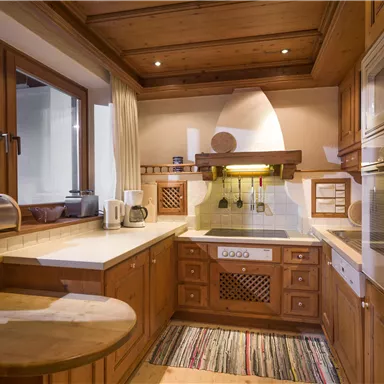 A modern wooden kitchen with light walls and large windows. The amenities include a stove, a sink, and a cozy corner with a small table.