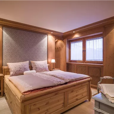 A cozy bedroom with wooden walls and a large double bed. Soft lighting and windows with curtains create an inviting atmosphere.
