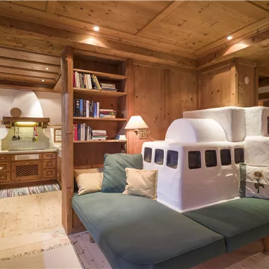 A cozy living kitchen with wooden shelves and warm lighting. In the foreground is a green sofa with a striking, sculptural element.