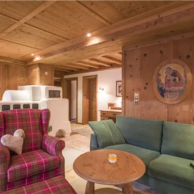 A cozy living space with a wooden ceiling and rustic furniture. A red armchair with a checked pattern and a green couch invite you to relax.