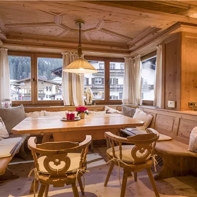 A cozy dining area made of wood with a large table and comfortable seating. Through the windows, one can see a winter landscape.