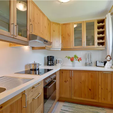 A bright kitchen with wooden furniture and modern appliances. Fresh flowers and various kitchen utensils are on the countertop.