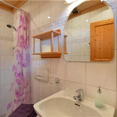 Ein modernes Badezimmer mit einem Waschbecken und einem großen Spiegel. Die Wände sind gefliest und eine Dusche ist mit einer Vorhangtrennwand ausgestattet.