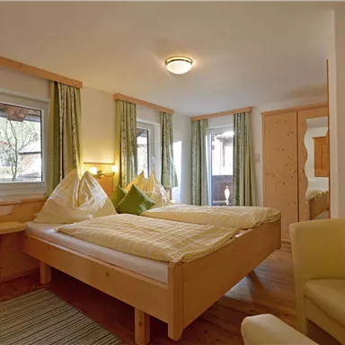 Ein gemütliches Zimmer mit zwei Betten und holzverkleideten Wänden. Helle Vorhänge und ein Sessel schaffen eine einladende Atmosphäre.
