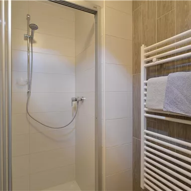 A modern bathroom with a shower and a towel warmer. The walls are light tiled, and there are fresh towels.
