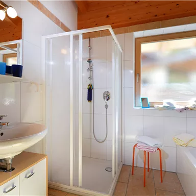 Ein modernes Badezimmer mit einer Duschkabine und einem Waschbecken. Ein Fenster sorgt für Tageslicht und es gibt einige Handtücher auf einer Ablage.