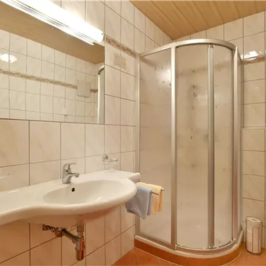 A modern bathroom with a shower cabin and a sink. The walls are tiled and the space is bright and clean.