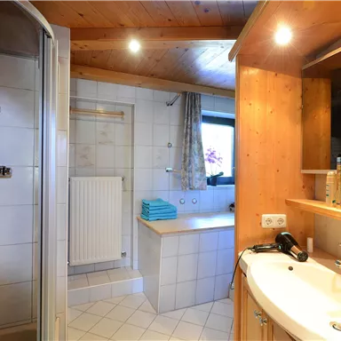 A modern bathroom with a shower and a sink. There are bright tiles and wood paneling, as well as towels on the shelf.