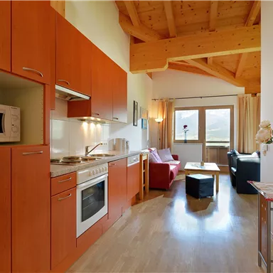 Eine moderne Küchenzeile mit Holzschränken und Heimelektronik. Der Wohnbereich ist hell und gemütlich, mit einem Sofa und Fenster, die Tageslicht hereinlassen.