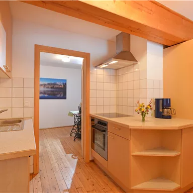 Eine moderne Küche mit Holzregalen und einem offenen Raum. Die Wände sind hell gefliest, und es gibt eine kleine Blumendekoration auf der Arbeitsplatte.